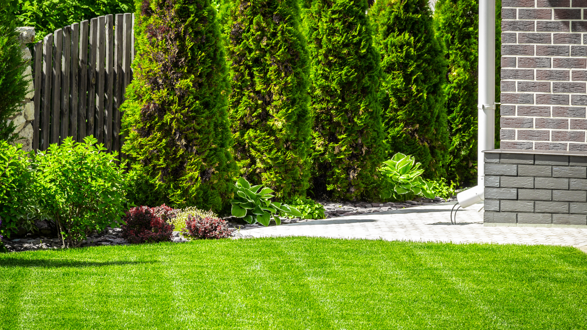 Lush green lawn with a pathway, landscaping, and a brick wall.