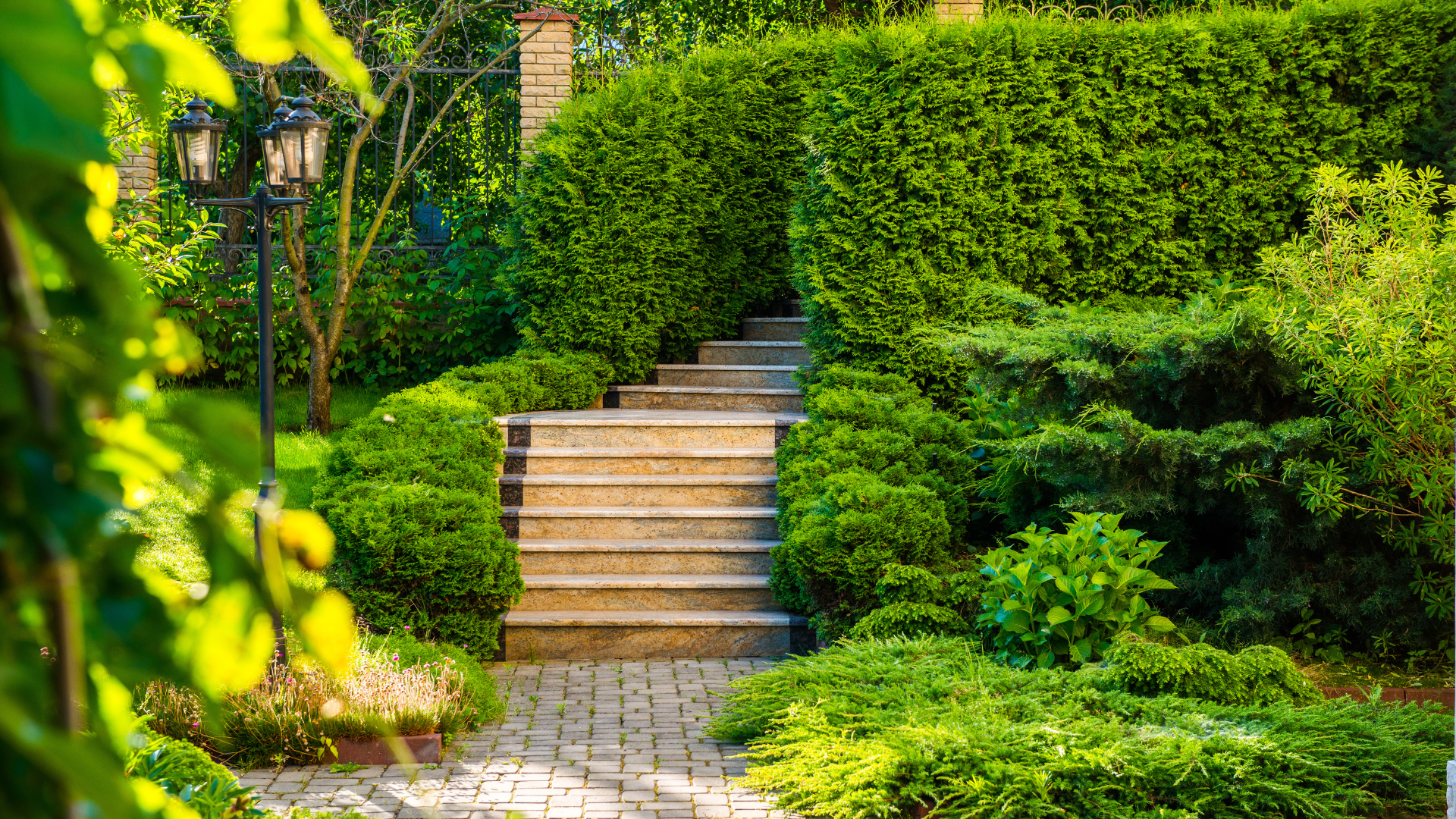 Stone steps ascend through a lush, green garden with manicured hedges and a lamppost.
