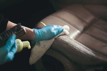 A Person Wearing Blue Gloves Is Cleaning a Leather Seat in A Car — Townsville Car Care Centre in Aitkenvale, QLD