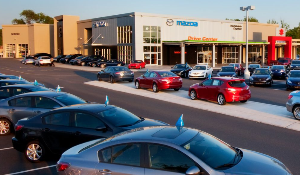 Cars parked at a Mazda dealership with a modern building and Drive Center sign.