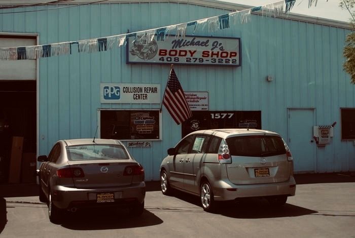 A blue building with a Michael's Body Shop sign, an American flag, and a Collision Repair Center sign.