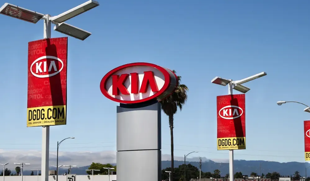 KIA dealership sign with red logo on a cylindrical post and red banners.