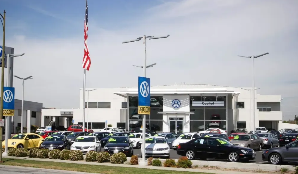Volkswagen car dealership with cars on display, blue and white building, sunny day.