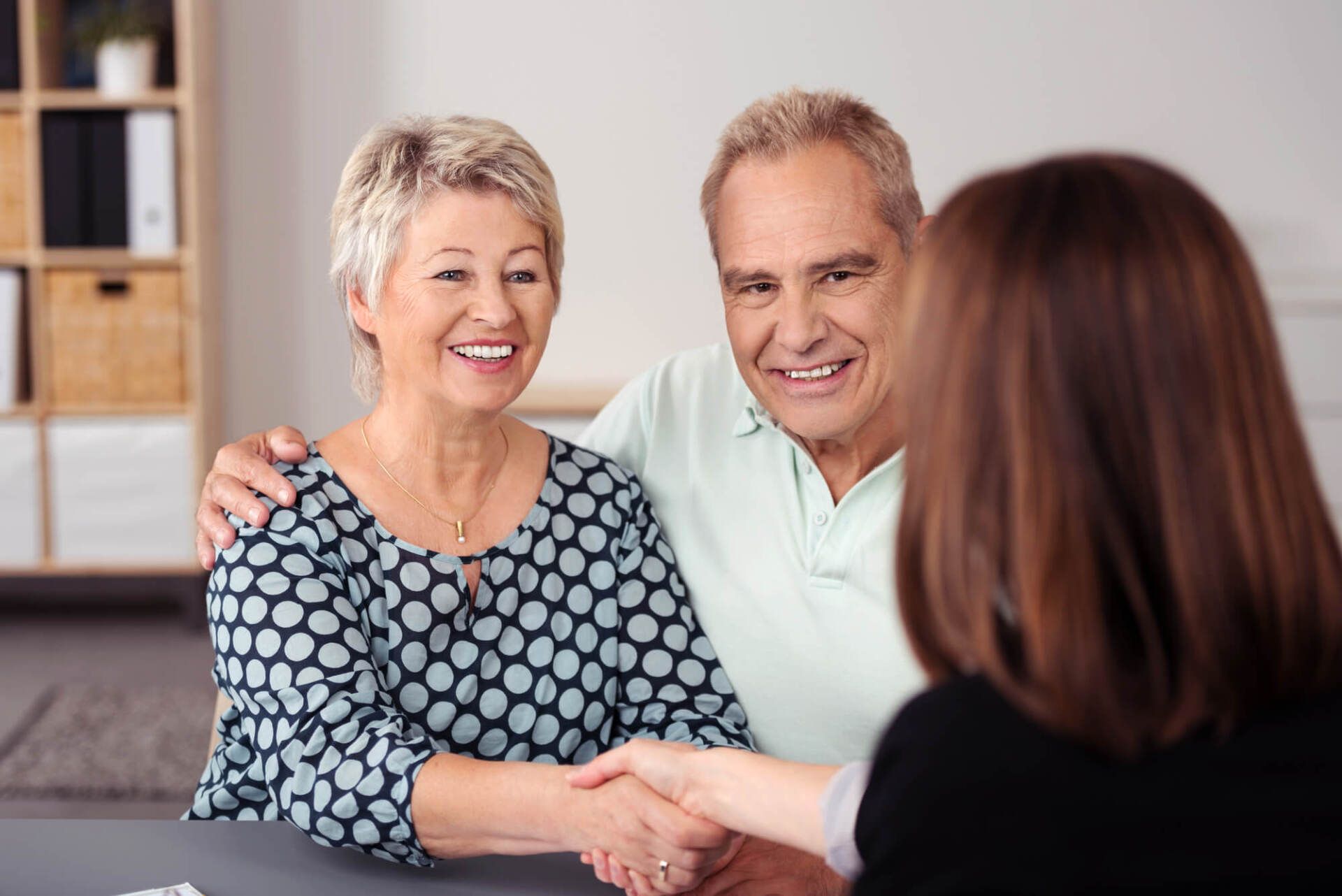 An elderly couple is shaking hands with a woman while sitting at a table.