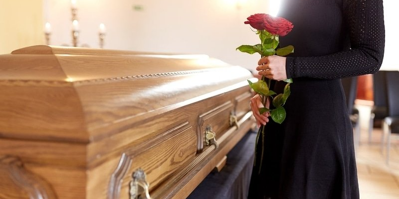 A woman is holding a rose in front of a coffin at a funeral.