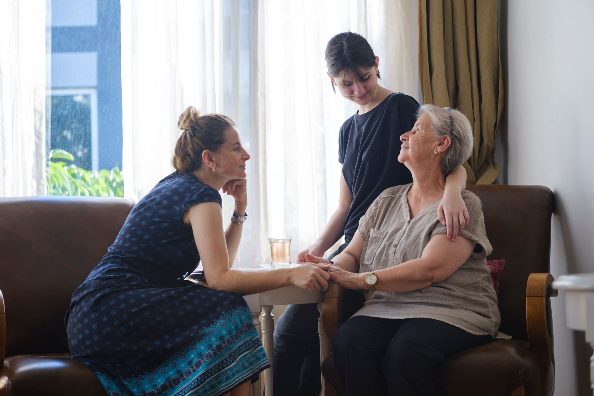 Three women are sitting on a couch holding hands and talking to each other.
