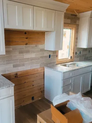 Kitchen under construction with white cabinets, wood and tile backsplash, and granite countertops.