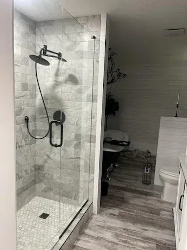 Modern bathroom with glass shower, gray tiled walls, and black fixtures.