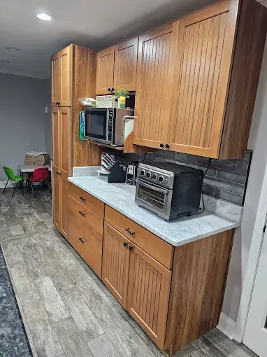 Kitchen with wood cabinets, countertop, and appliances; small children's play area visible in the background.