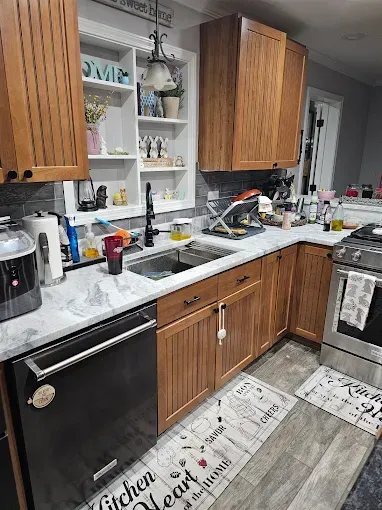 Kitchen with light wood cabinets, dark appliances, and a farmhouse-style sink, window shelves with decor.