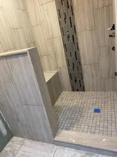 Bathroom shower with gray and white tile; bench and mosaic floor.