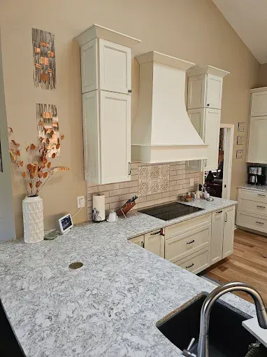 Cream-colored kitchen with quartz countertops, stovetop, and cabinets. A decorative backsplash and copper artwork.