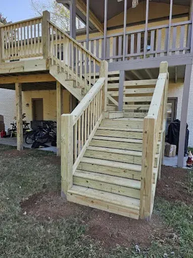 Wooden deck and staircase leading to a second-story porch, built outside a beige house.
