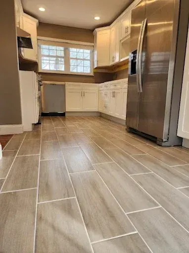 Kitchen with light wood-look tile floor, white cabinets, stainless steel refrigerator, and window.