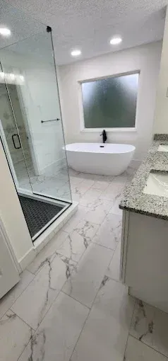 Modern bathroom with marble tile, glass shower, freestanding tub, and vanity.