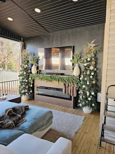 Outdoor Christmas scene with decorated trees, fireplace, TV, sofa on a wooden deck.