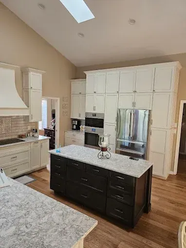 Modern kitchen with white cabinets, dark island, stainless steel appliances, and light wood floors.
