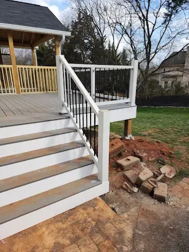 Deck with white stairs and railings, black metal balusters, and a covered wooden patio in the background.
