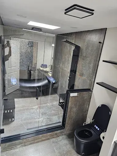 Modern bathroom with black toilet, shower, gray stone walls, and glass door.