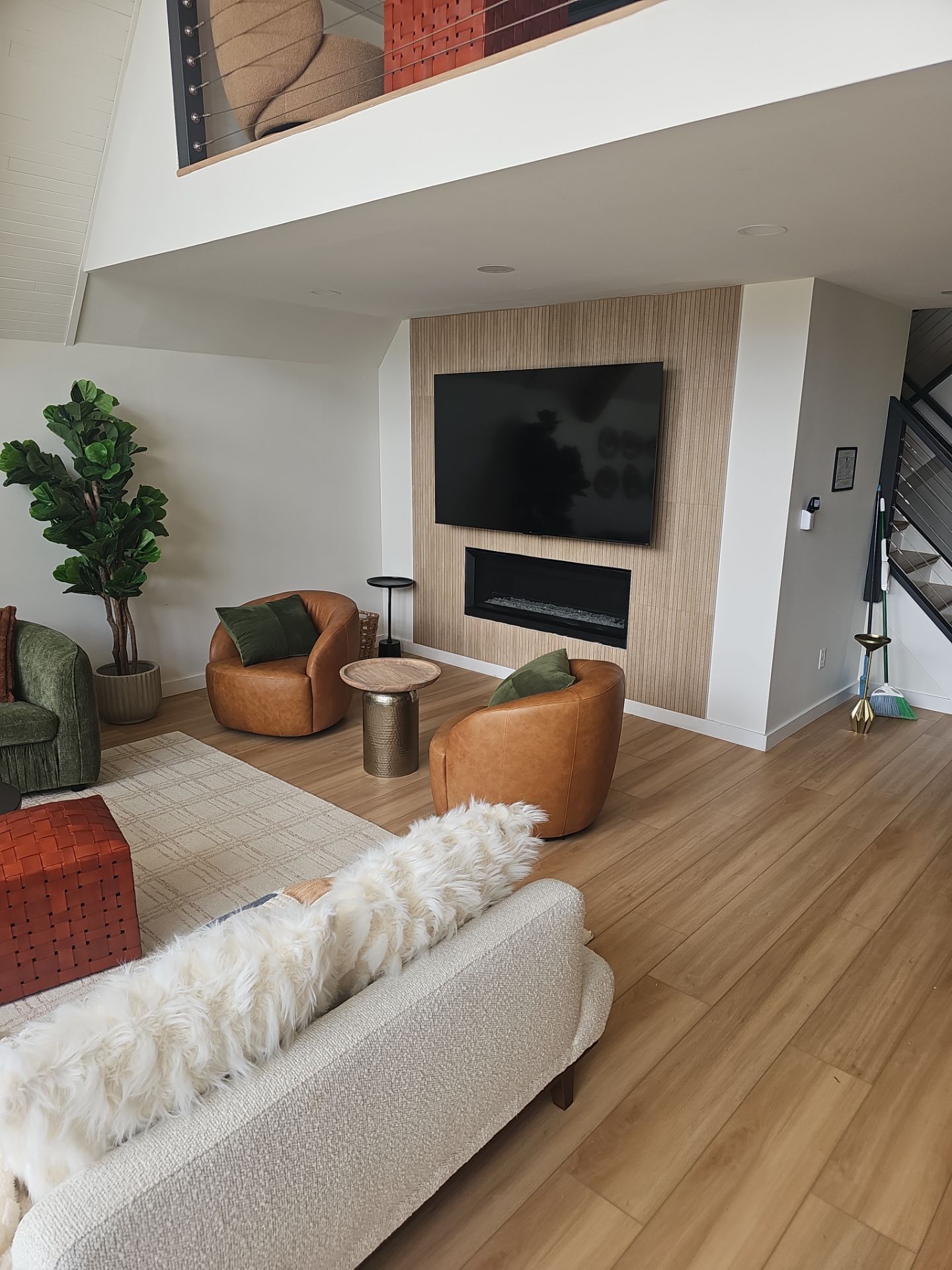 Cozy living room with light wood floors, TV above fireplace, two brown leather chairs, and a white couch.