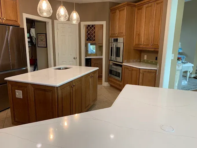 Kitchen with island and countertops, light wood cabinets, stainless steel appliances, and pendant lights.