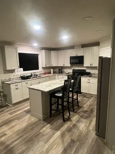 Modern kitchen with light cabinets, island with bar stools, stainless steel fridge, and wood-look flooring.