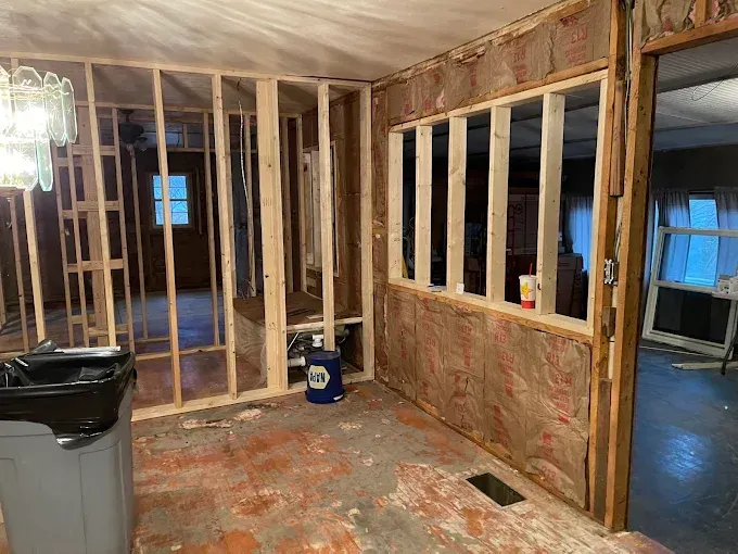 Interior room under construction, with exposed framing, insulation, and debris on the floor.