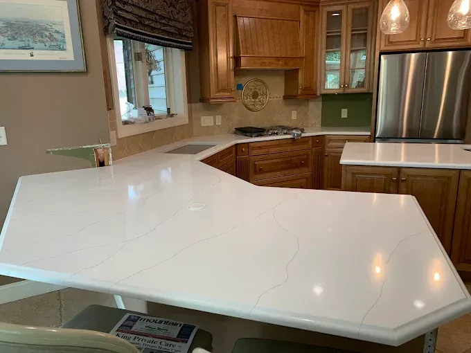 A bright white quartz countertop in a kitchen with wooden cabinets and a stainless steel refrigerator.