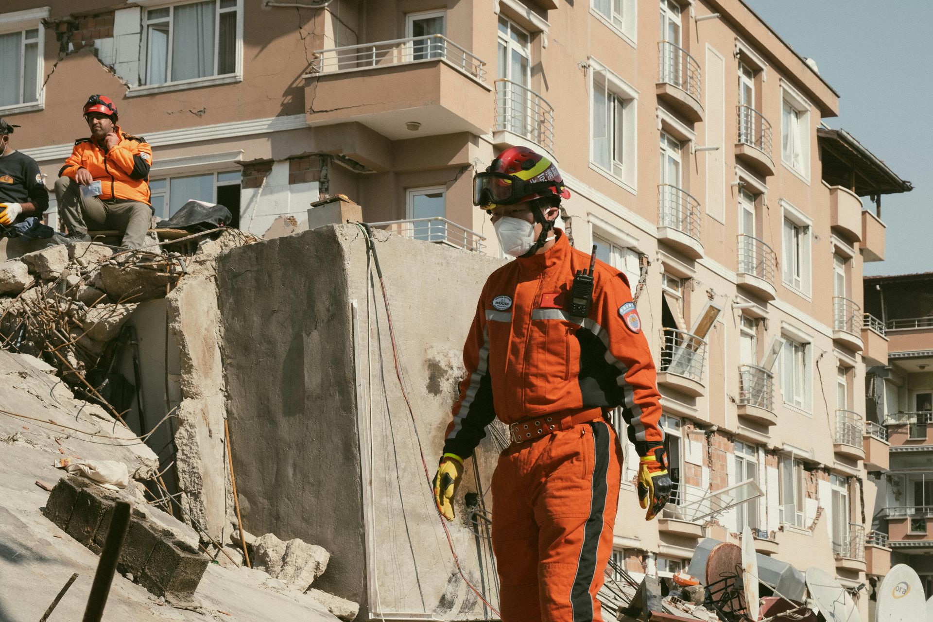 Rescue worker in orange suit at a collapsed building site, surveying the damage.