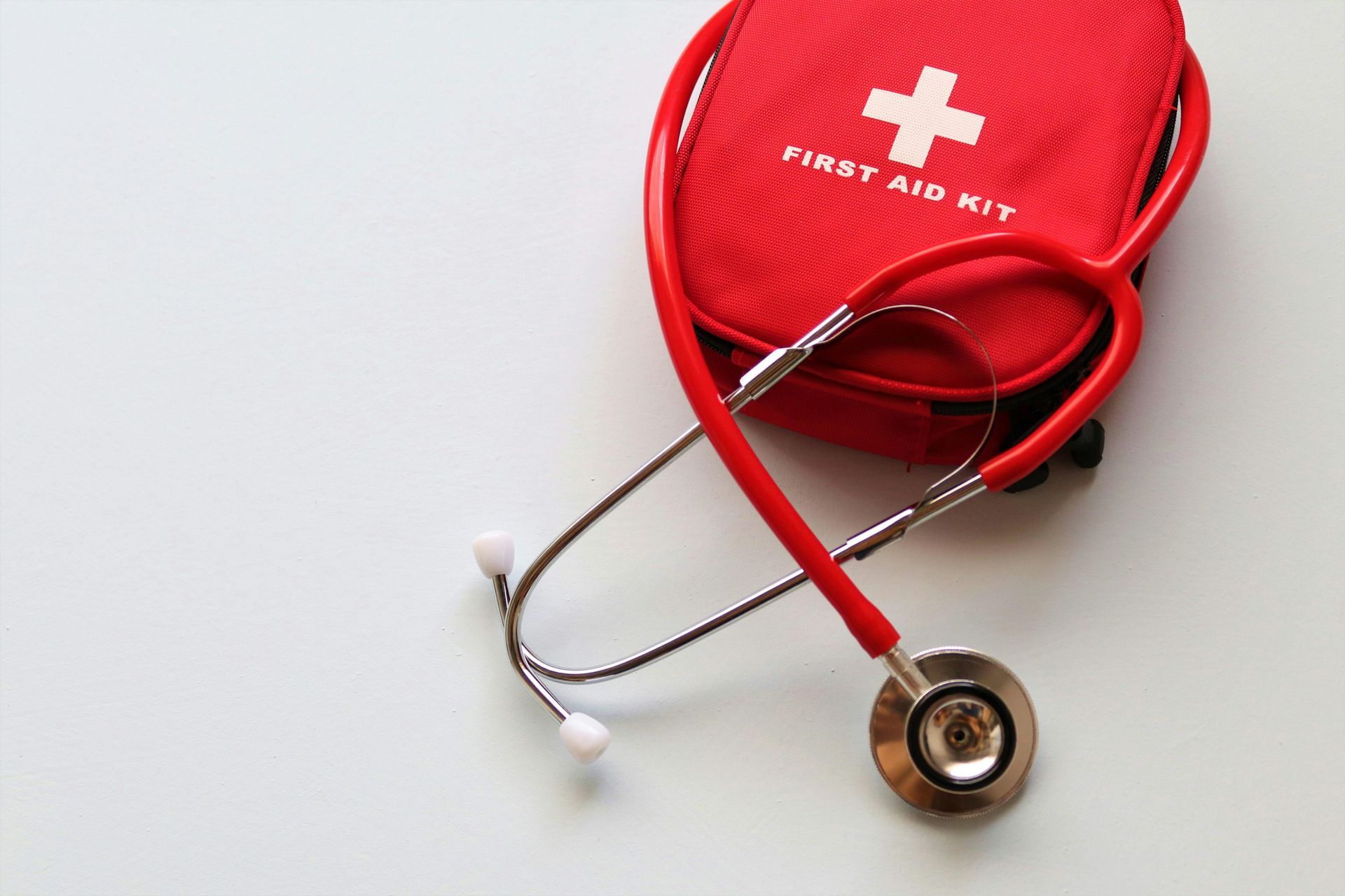 Red first aid kit and stethoscope on white surface.