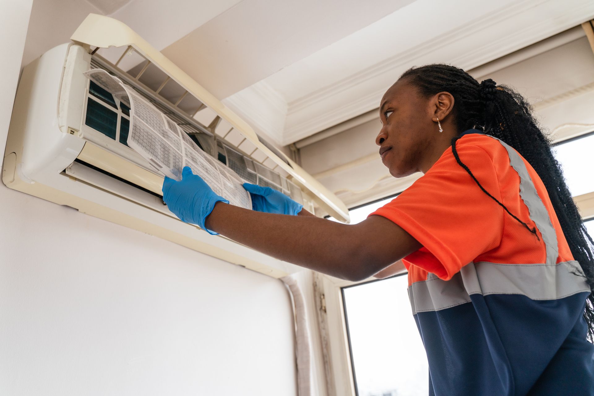 Technician in gloves adjusts AC filter near window during maintenance.