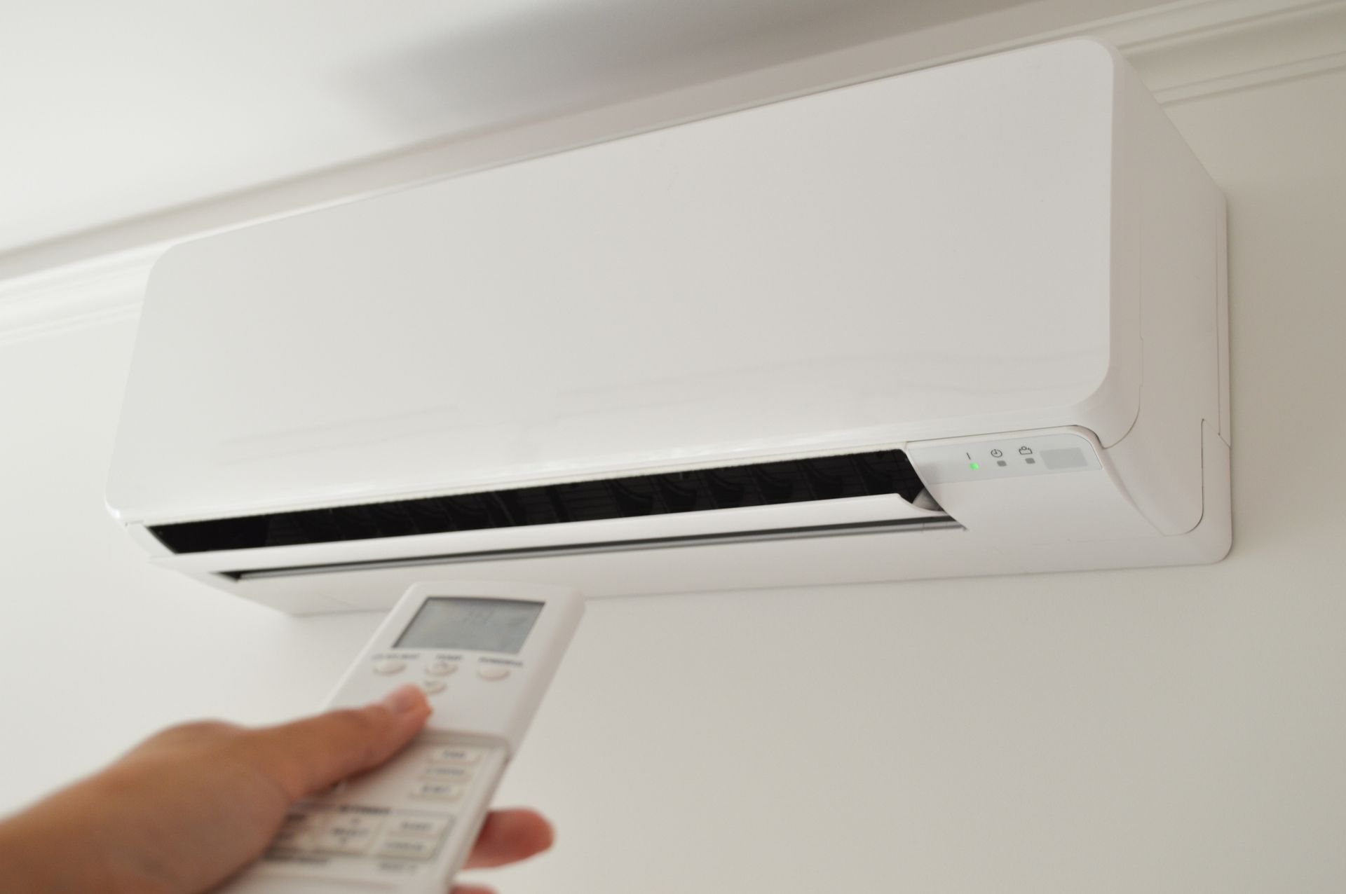Hand aiming remote control at wall-mounted air conditioner. Hand aiming remote control at wall-mounted air conditioner.