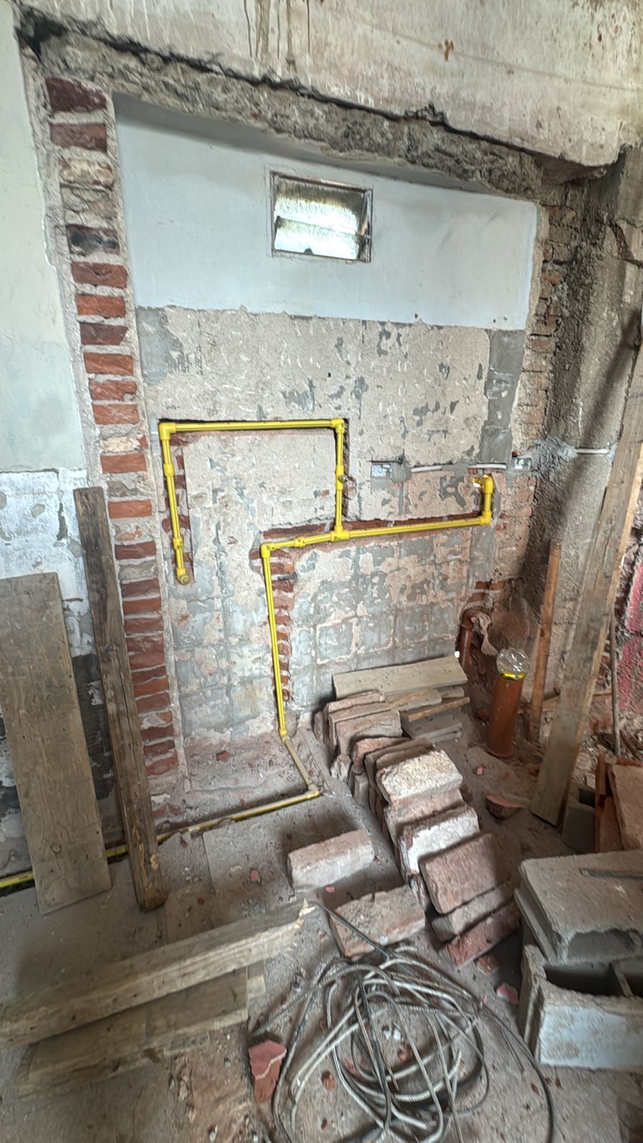 Las tuberías de gas de color amarillo corren a lo largo de una pared de ladrillo y hormigón en un entorno de construcción.