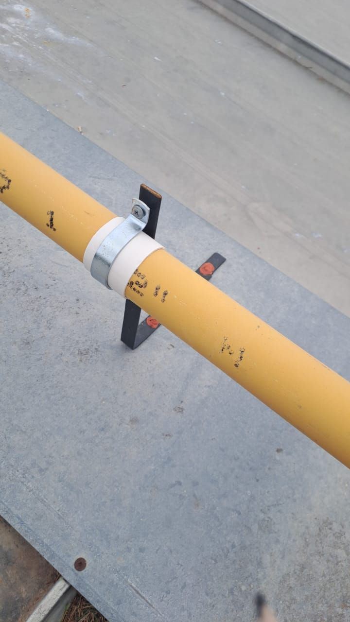 Tubo amarillo sujeto por una abrazadera metálica y un soporte negro sobre una superficie gris.