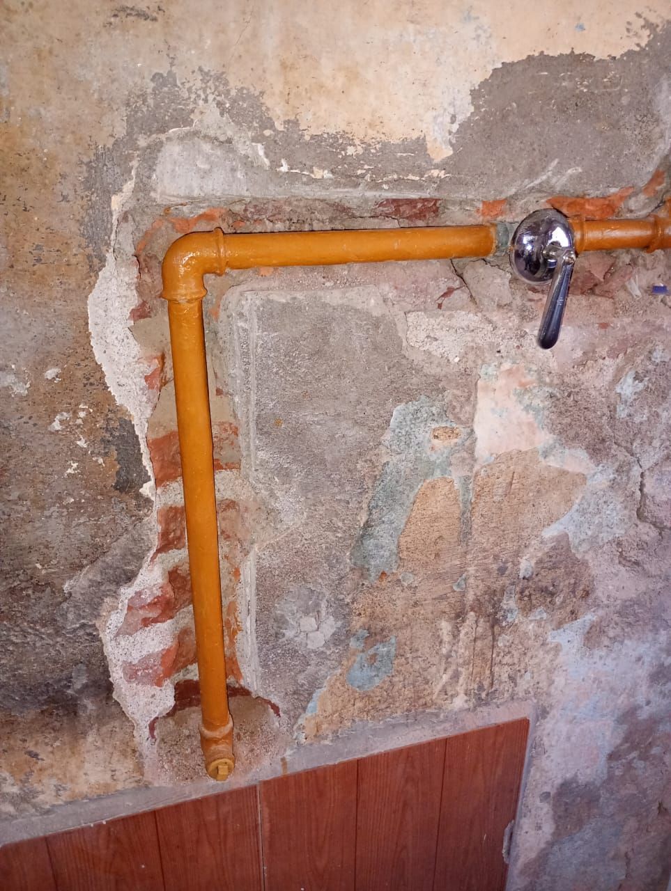 Tuberías de agua de color naranja en una pared dañada con una válvula