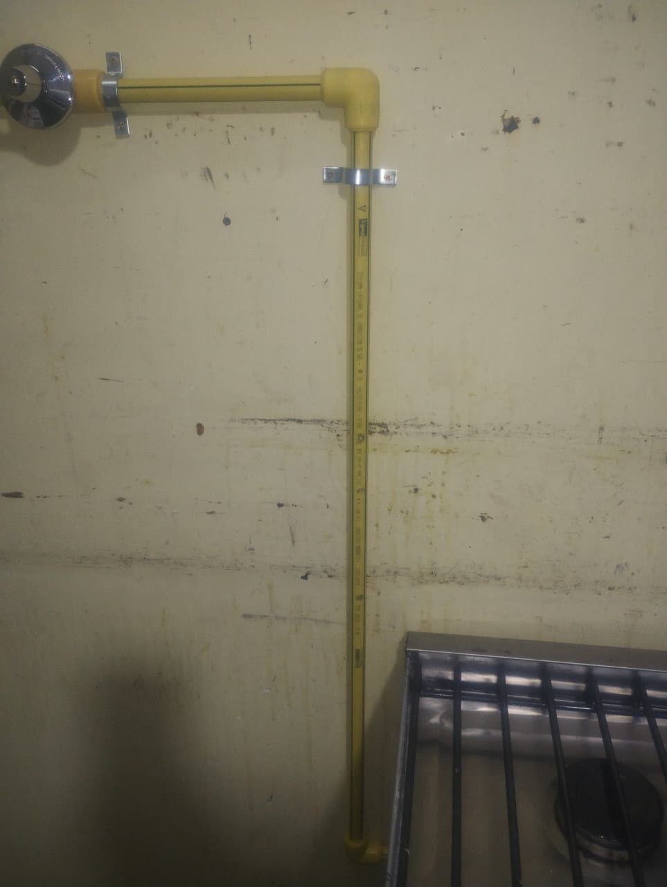 Tubería de gas amarilla en la pared que conecta con una estufa. Soportes metálicos la sujetan.