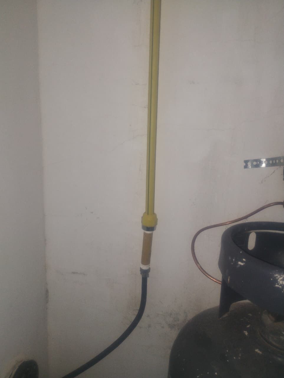 Manguera de gas amarilla conectada a una manguera negra y a un tanque de gas, montado en una pared blanca.