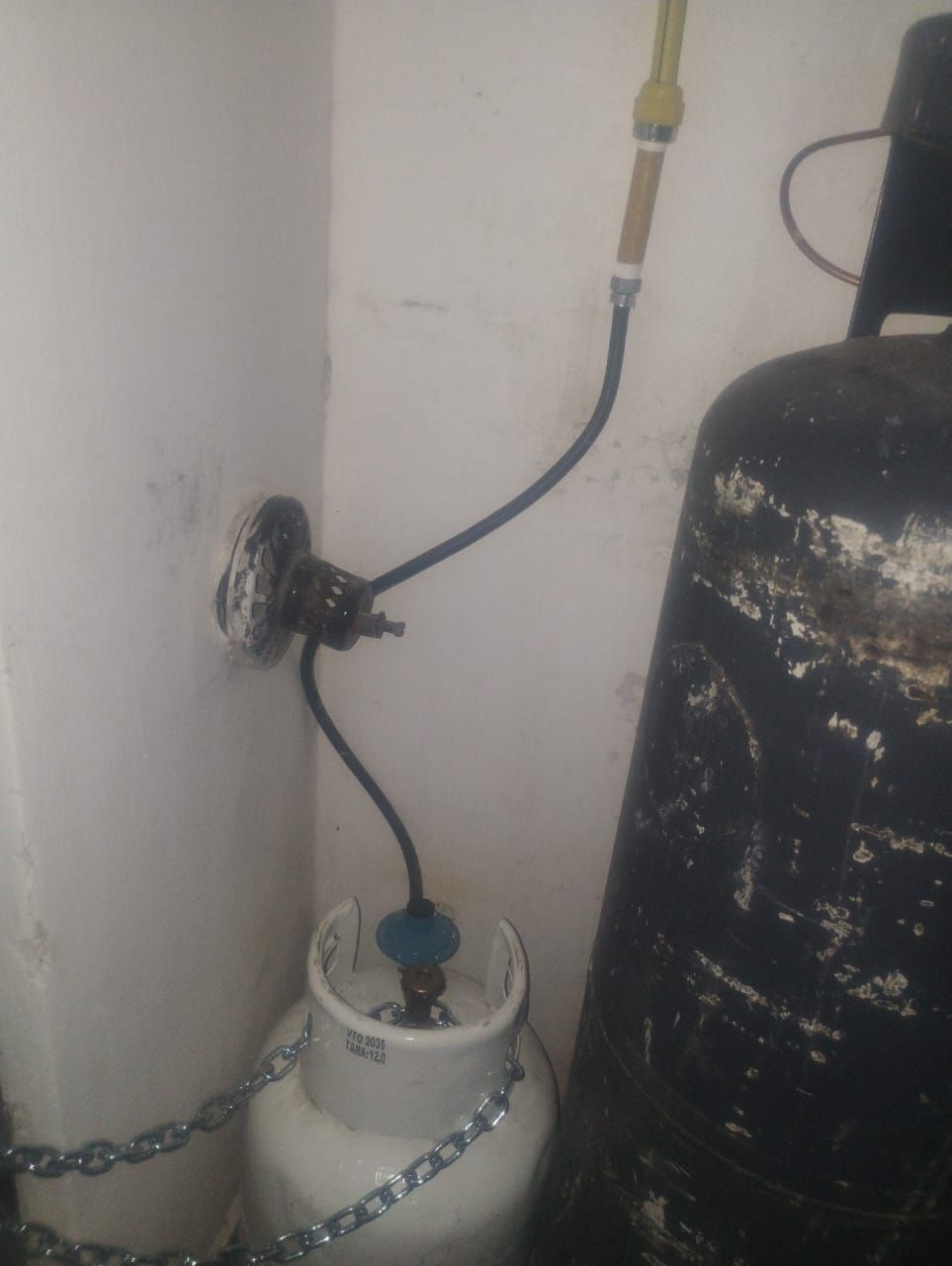 Tanques de gas conectados a una toma de pared mediante mangueras y un regulador.