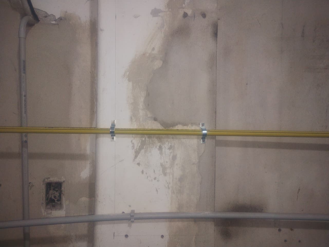 Pared con manchas de agua, conducto eléctrico y cables amarillos asegurados con clips.