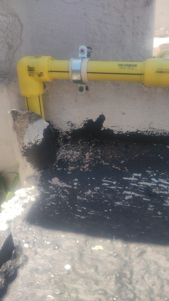 Tubo de gas amarillo fijado a una pared con una abrazadera de metal, apoyado sobre una superficie oscura.