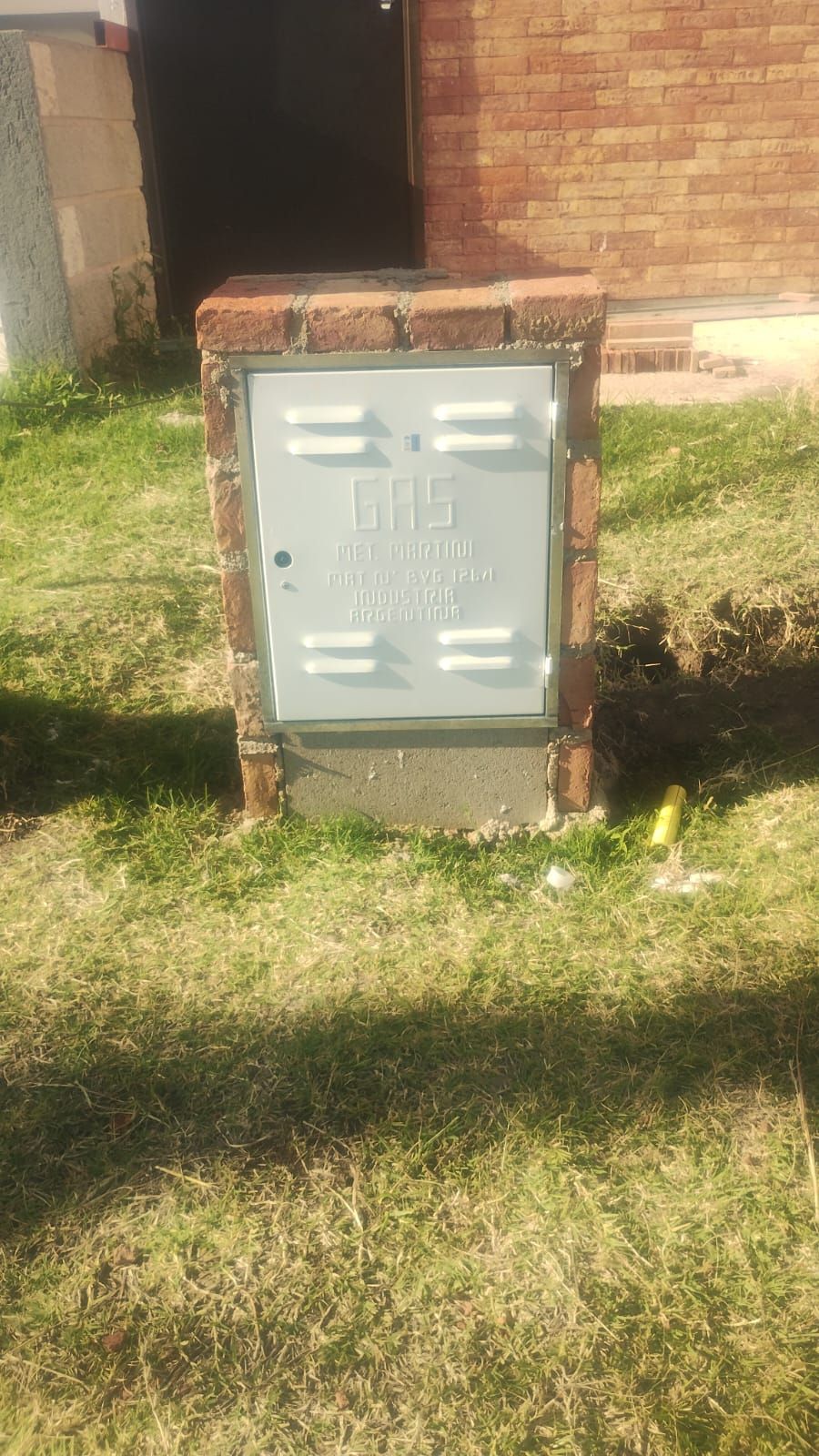 Caja de servicios públicos revestida de ladrillo con puerta de metal colocada sobre una base de hormigón 