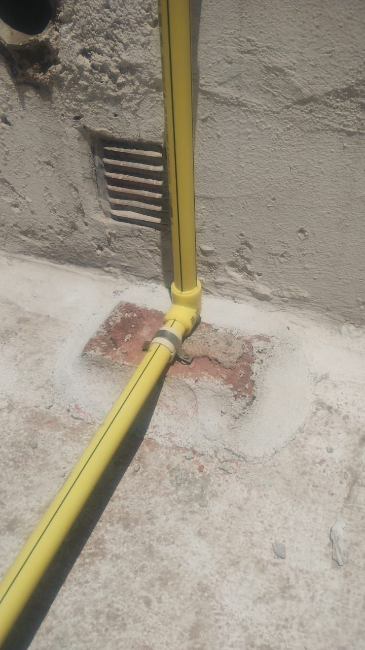 Tubería de gas amarilla contra una pared y suelo de hormigón, con un parche de ladrillo.
