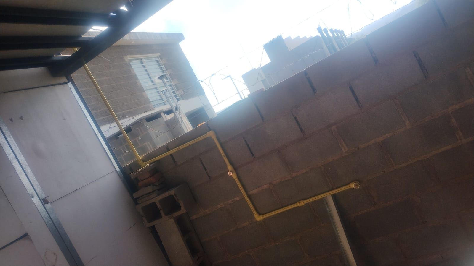 Tuberías de gas amarillas recorren una pared de bloques de hormigón gris. Al fondo se ve un edificio a medio construir.