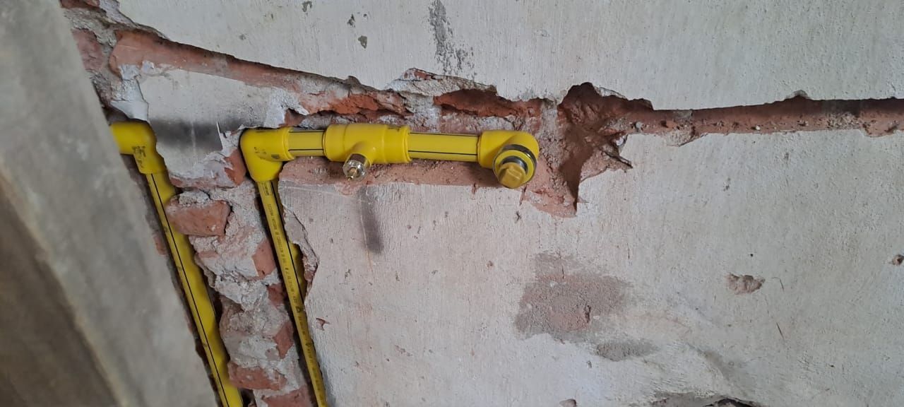 Tuberías amarillas encapsuladas en una pared de ladrillo tosco y yeso.