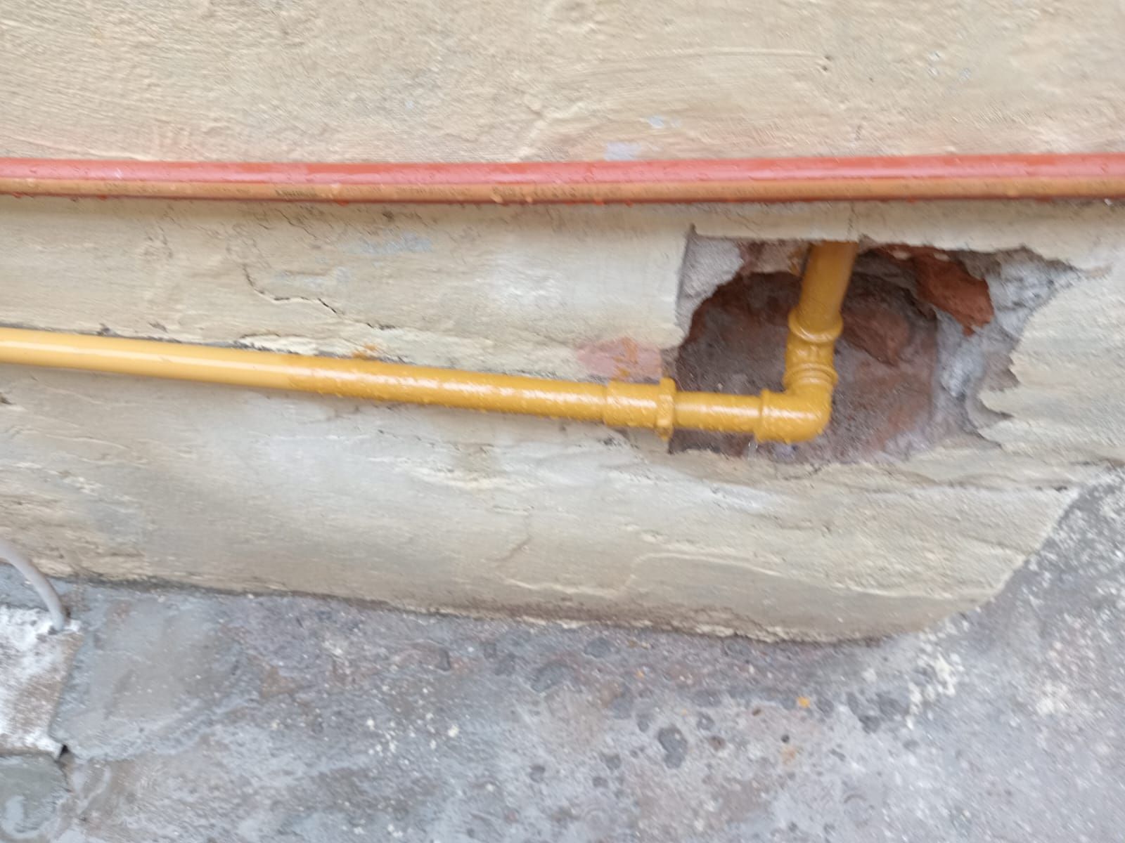 Tubería de gas amarilla que sobresale de la pared de un edificio dañado.