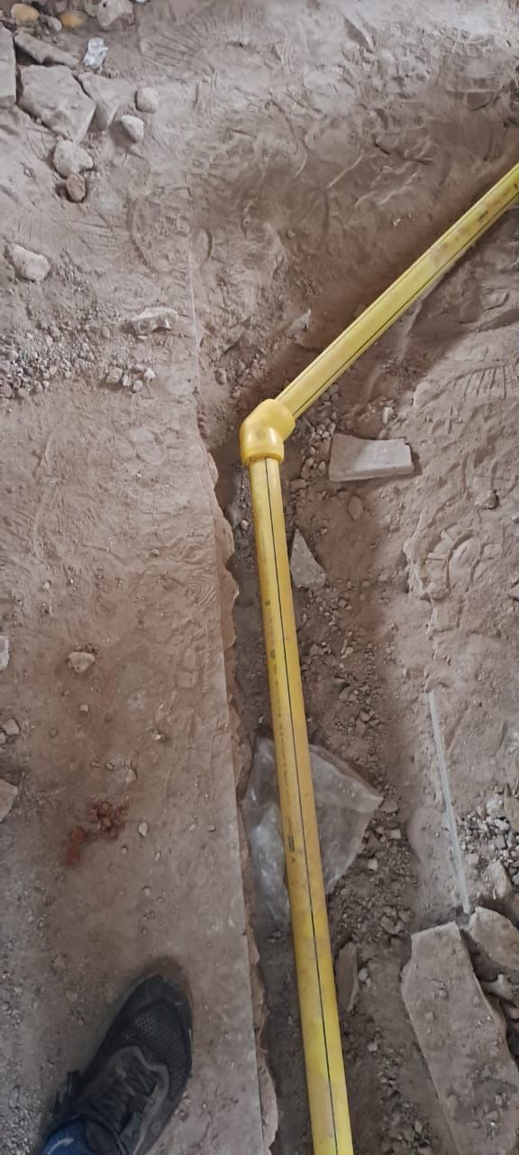 Tubo de gas amarillo que corre por una zanja en el suelo, mostrando la articulación del codo y el pie de una persona.