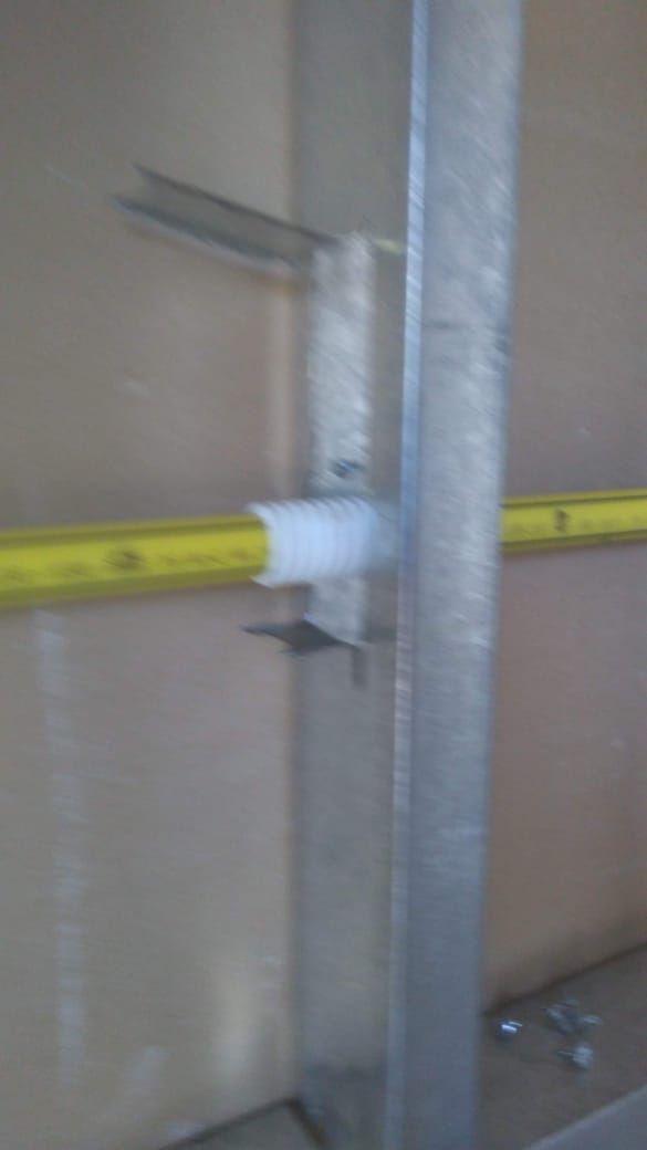 Conducto eléctrico amarillo fijado a un montante metálico con un accesorio de plástico blanco.