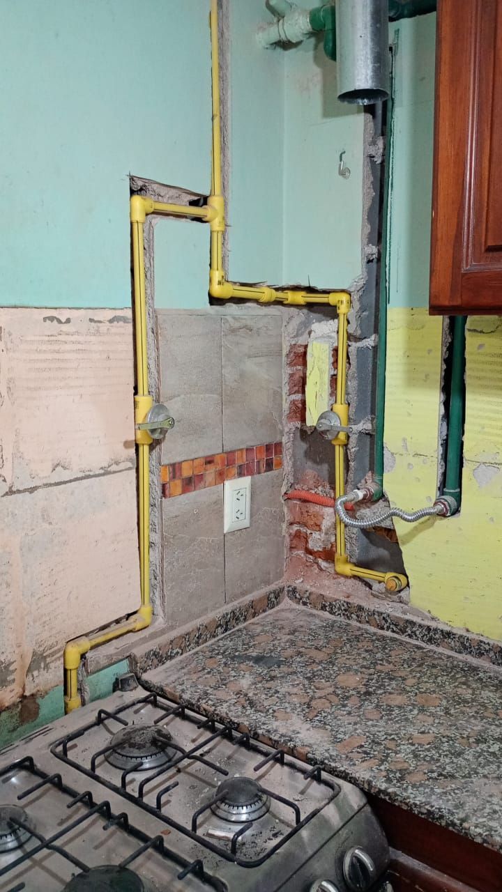 Conductos de gas de cocina, tuberías amarillas, contra una pared verde azulado, con una estufa