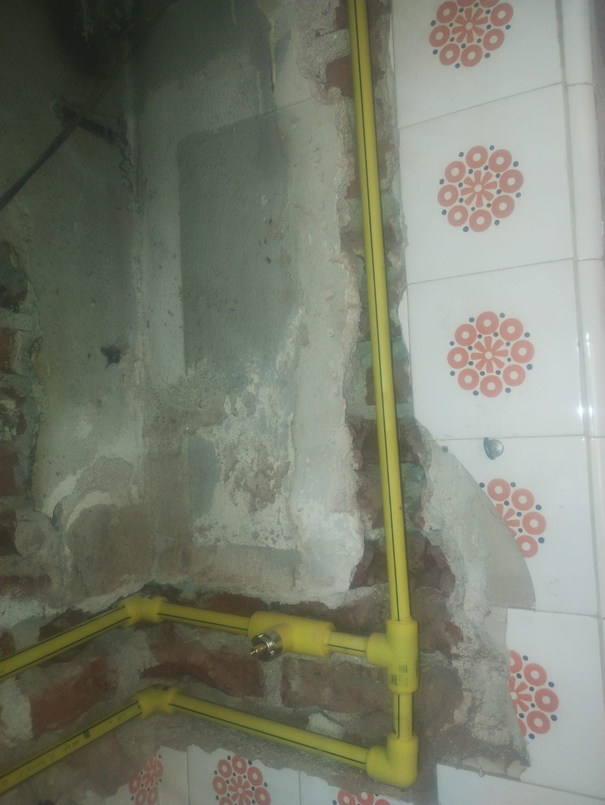 Tuberías de gas amarillas instaladas en una pared con ladrillos a la vista y azulejos estampados.