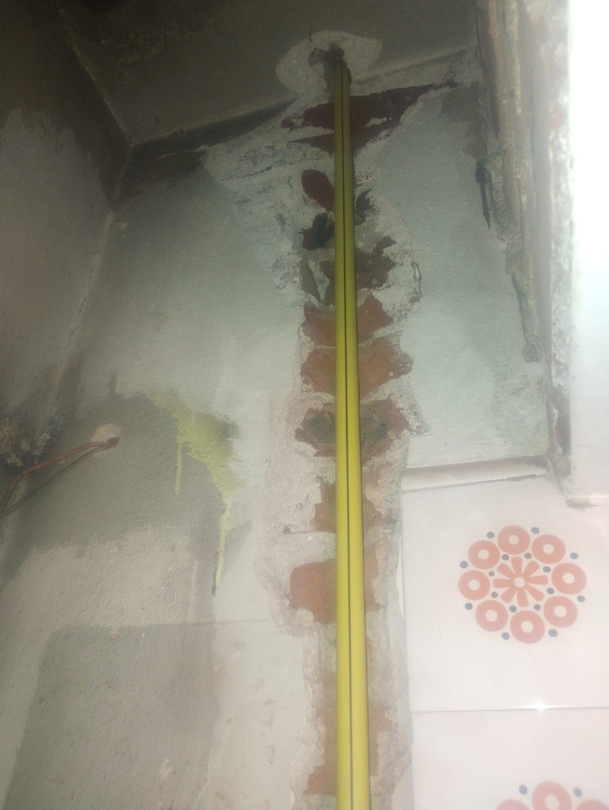 Pared interior dañada con ladrillos a la vista y tuberías amarillas. Se ven algunos azulejos a la derecha.